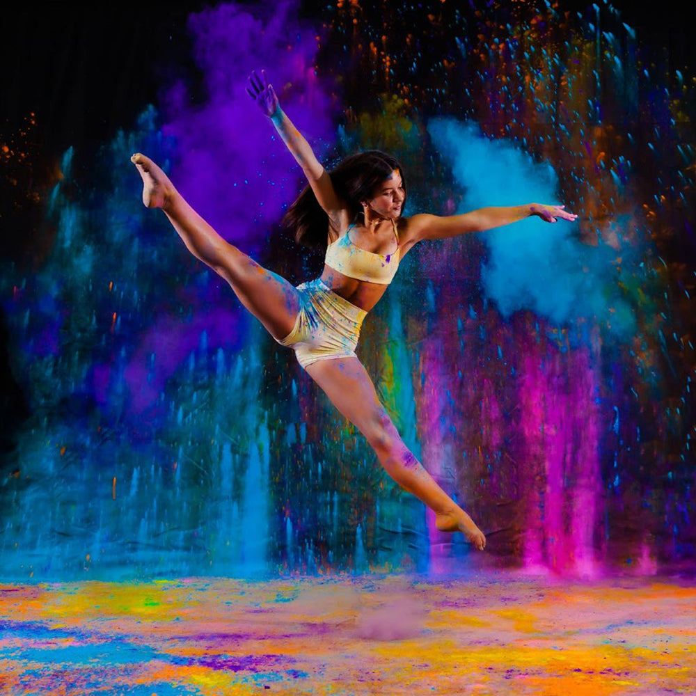 A dancer mid-leap surrounded by vibrant colored powder clouds.