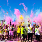 Group of people celebrating a colorful 5K run with pink, yellow, and blue powder in the air.