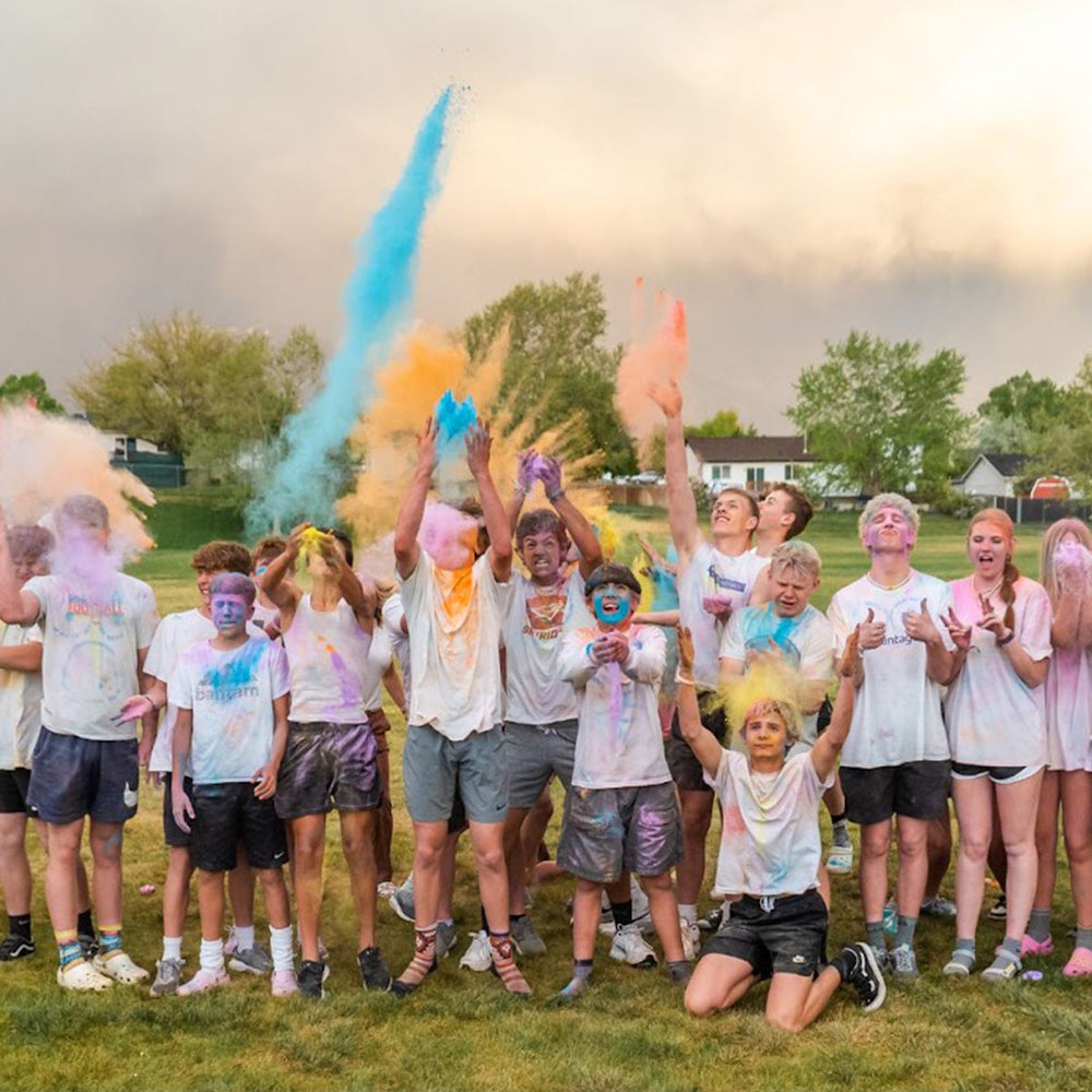 Group of people celebrating with colorful powder in an outdoor setting.