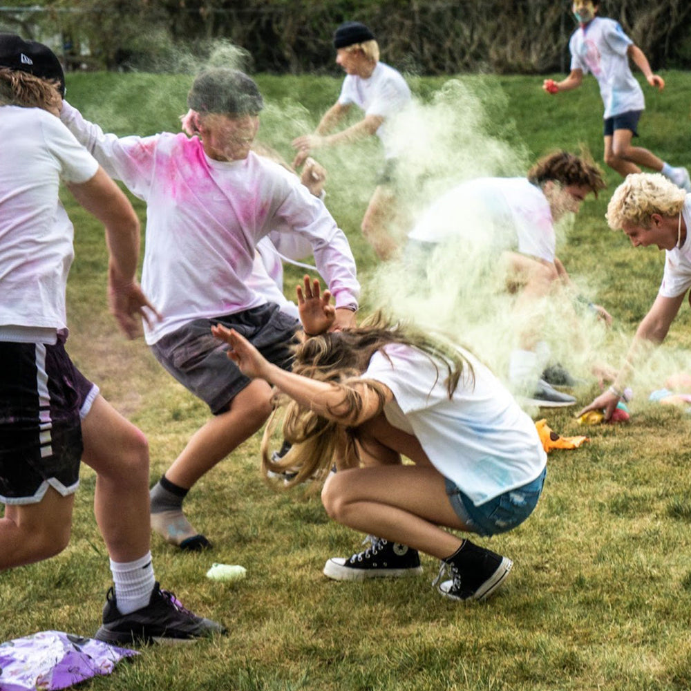 Group of people playing a colorful powder fight game on a grassy field.