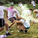 Group of people playing a colorful powder fight game on a grassy field.