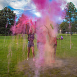 People celebrating with pink powder in a grassy park.